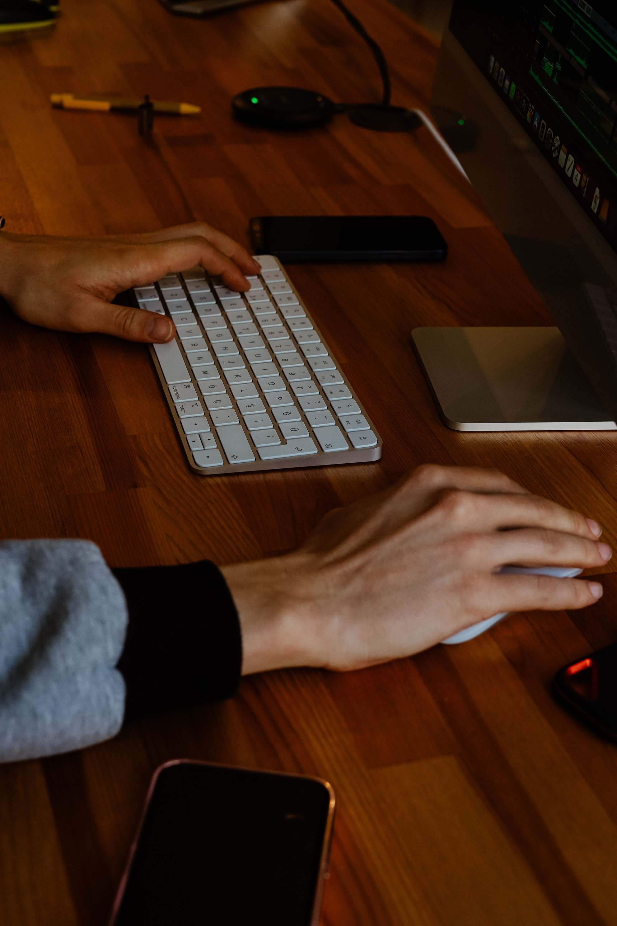 Close-up of hands typing on a keyboard beside a monitor on a modern desk